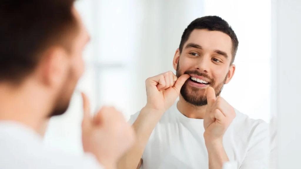Hombre pasándose el hilo dental frente el espejo para obtener una higiene bucodental completa
