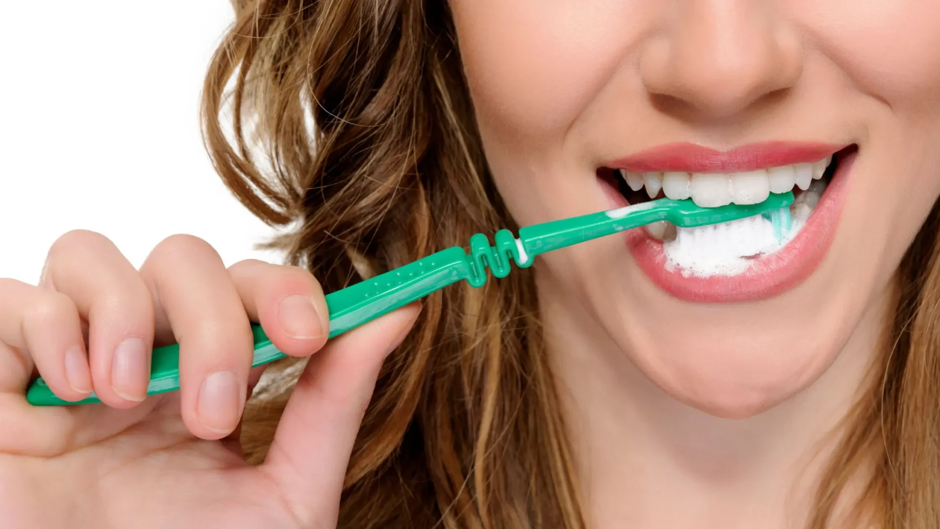 Mujer cepillándose los dientes a la vez que sonríe