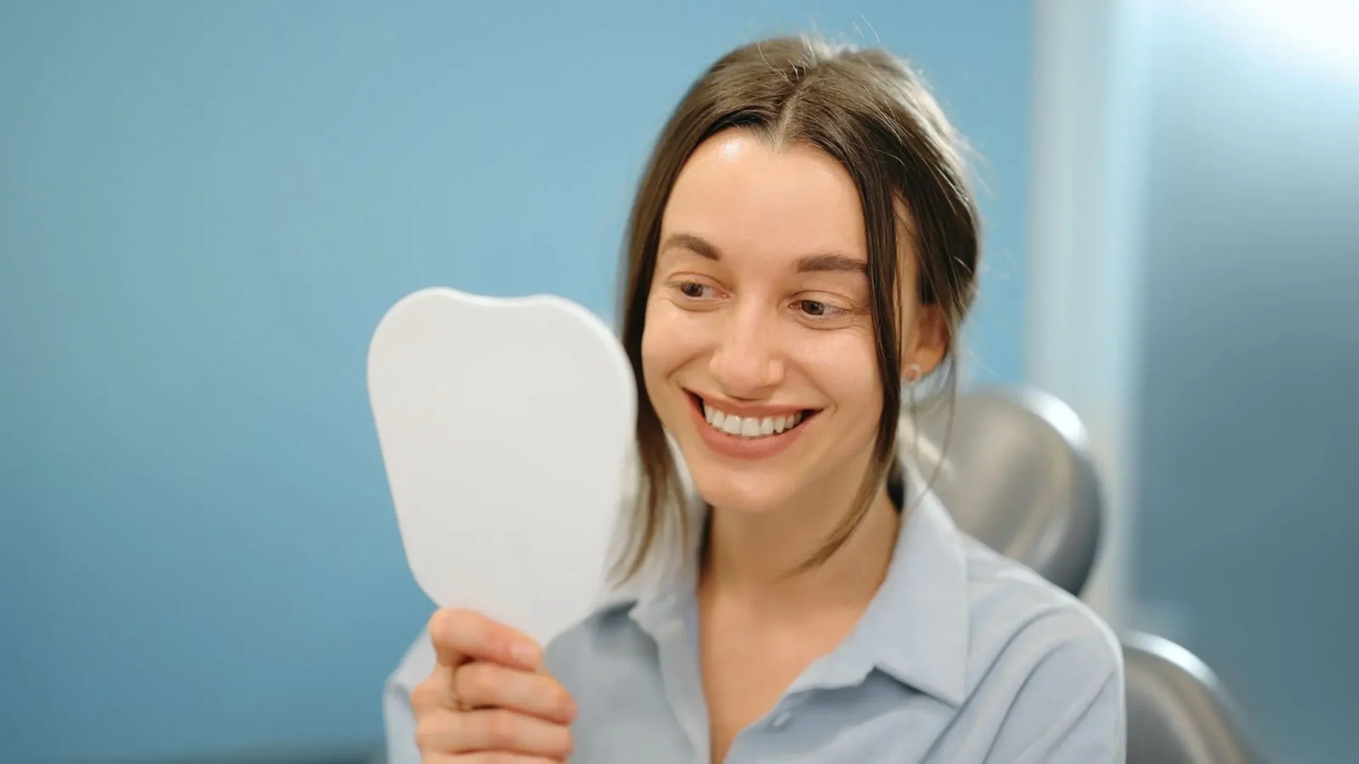 Mujer sonriendo frete a un espejo contemplando su sonrisa radiante por tener buenos hábitos al lavarse los dientes