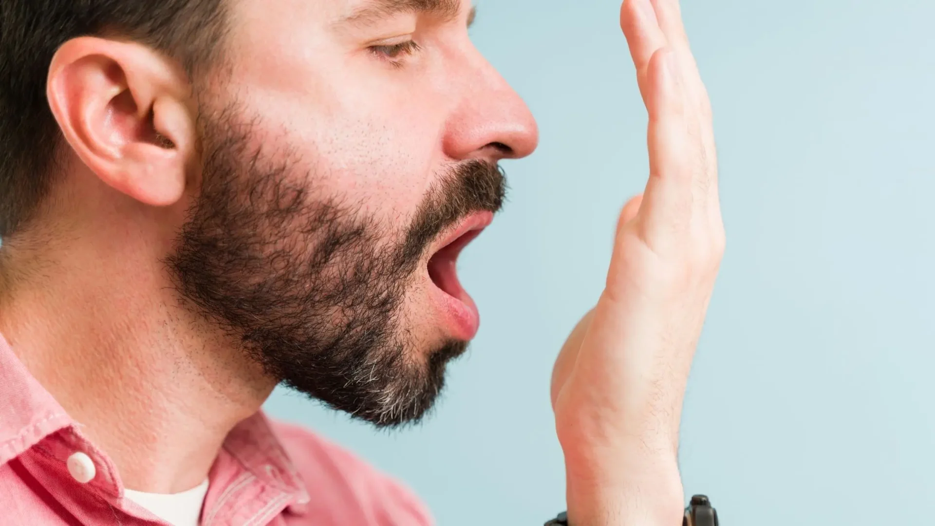 Hombre comprobando el olor de su aliento, una de las causas de la periodontitis